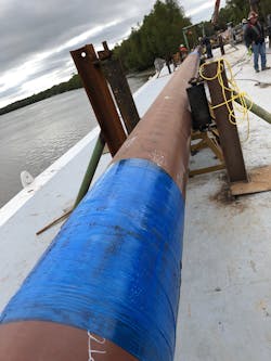 Technicians wrapped the pre-impregnated, tri-axial fiberglass laminate around the pipeline on the deck of a barge in preparation for installation. Technicians wrapped the pre-impregnated, tri-axial fiberglass laminate around the pipeline on the deck of a barge in preparation for installation.