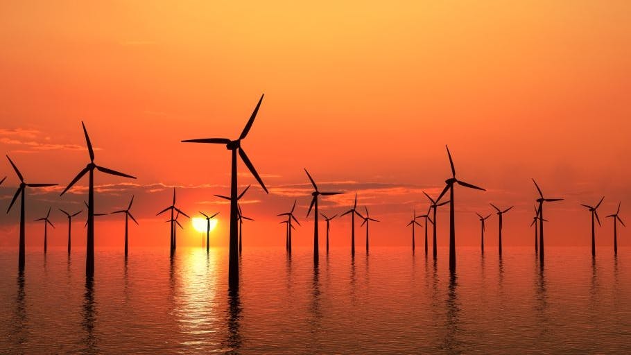 Wind turbines generating electricity offshore silhouetted by a golden sunset