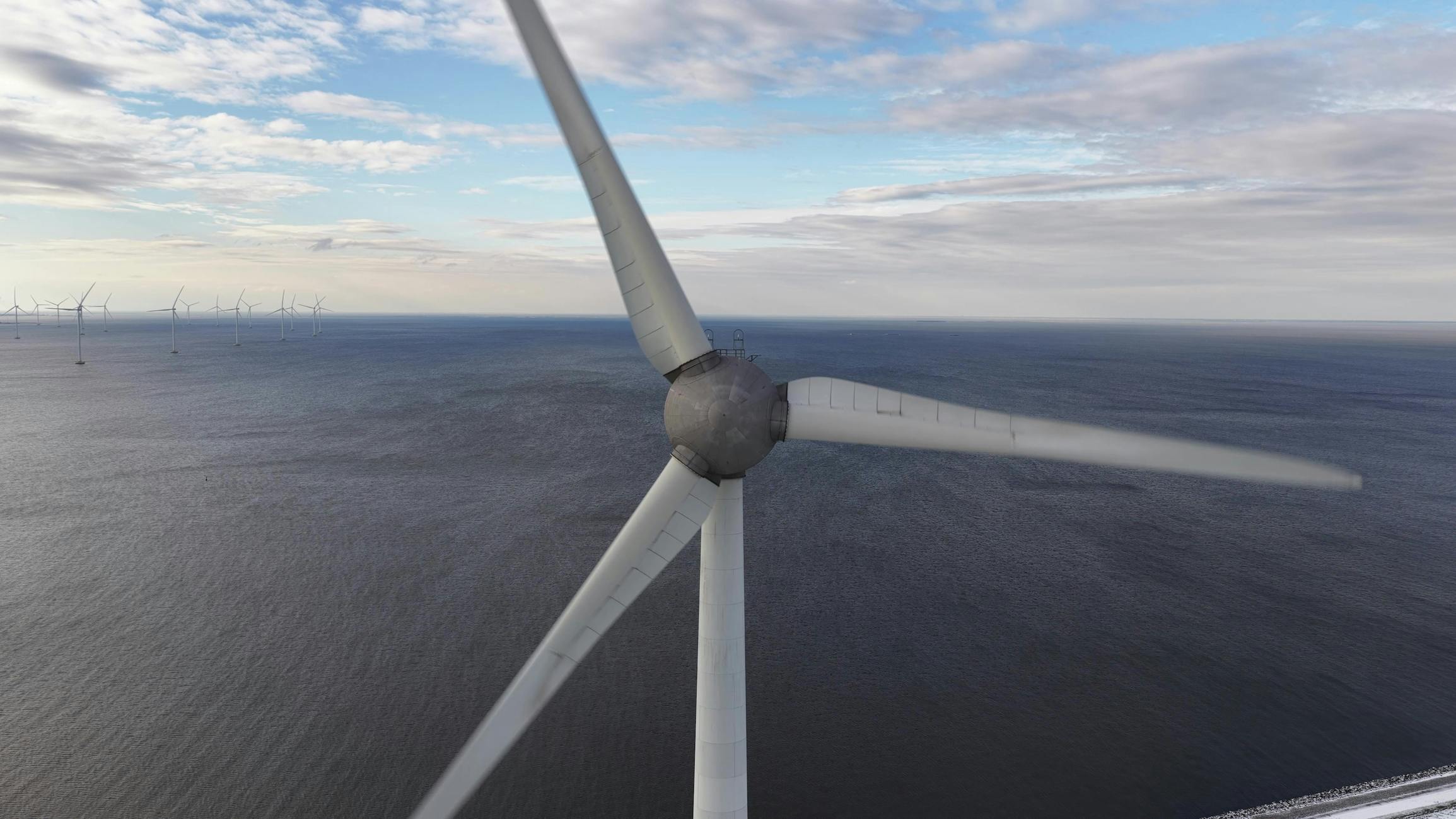 Close-up aerial perspective of a wind turbine spinning over the ocean